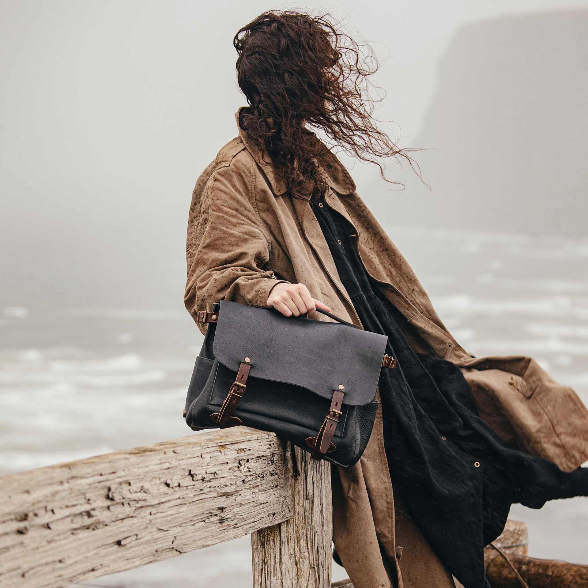 Une femme en bord de mer porte &agrave; la main sa besace en cuir bleu.