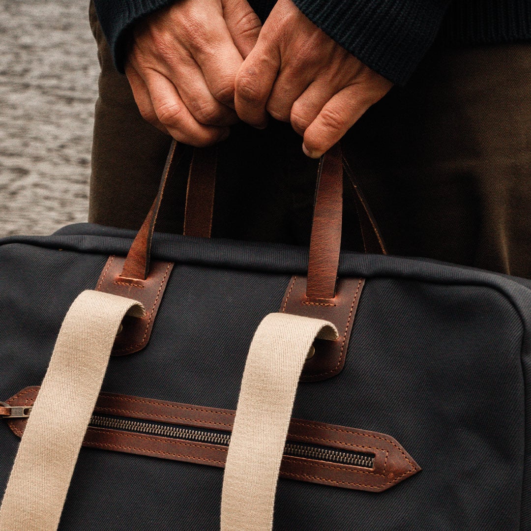 Gros plan sur les poign&eacute;es en cuir et la bandouillere coton du sac de voyage Missak