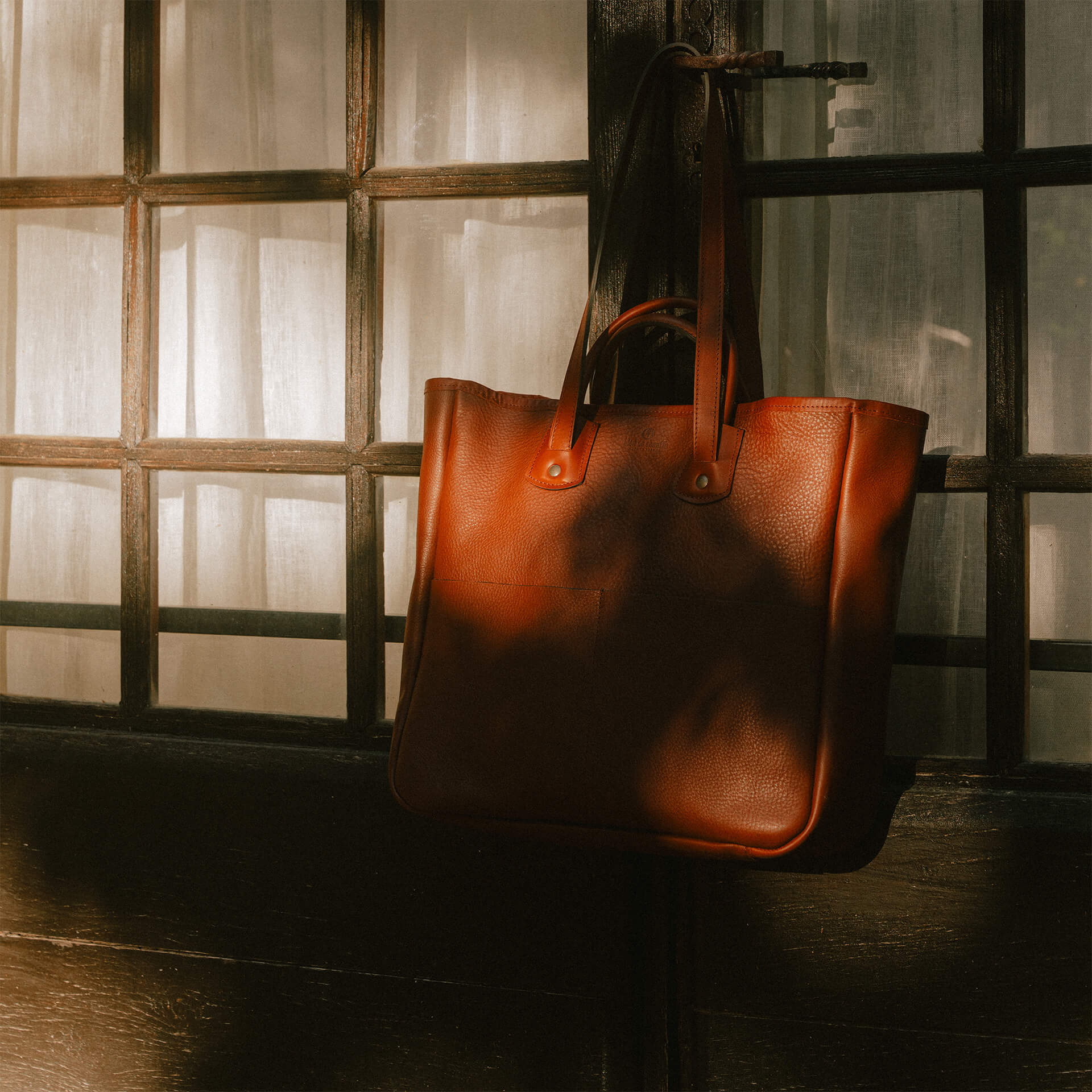 Bleu de Chauffe leather tote bag in front of a wood window.