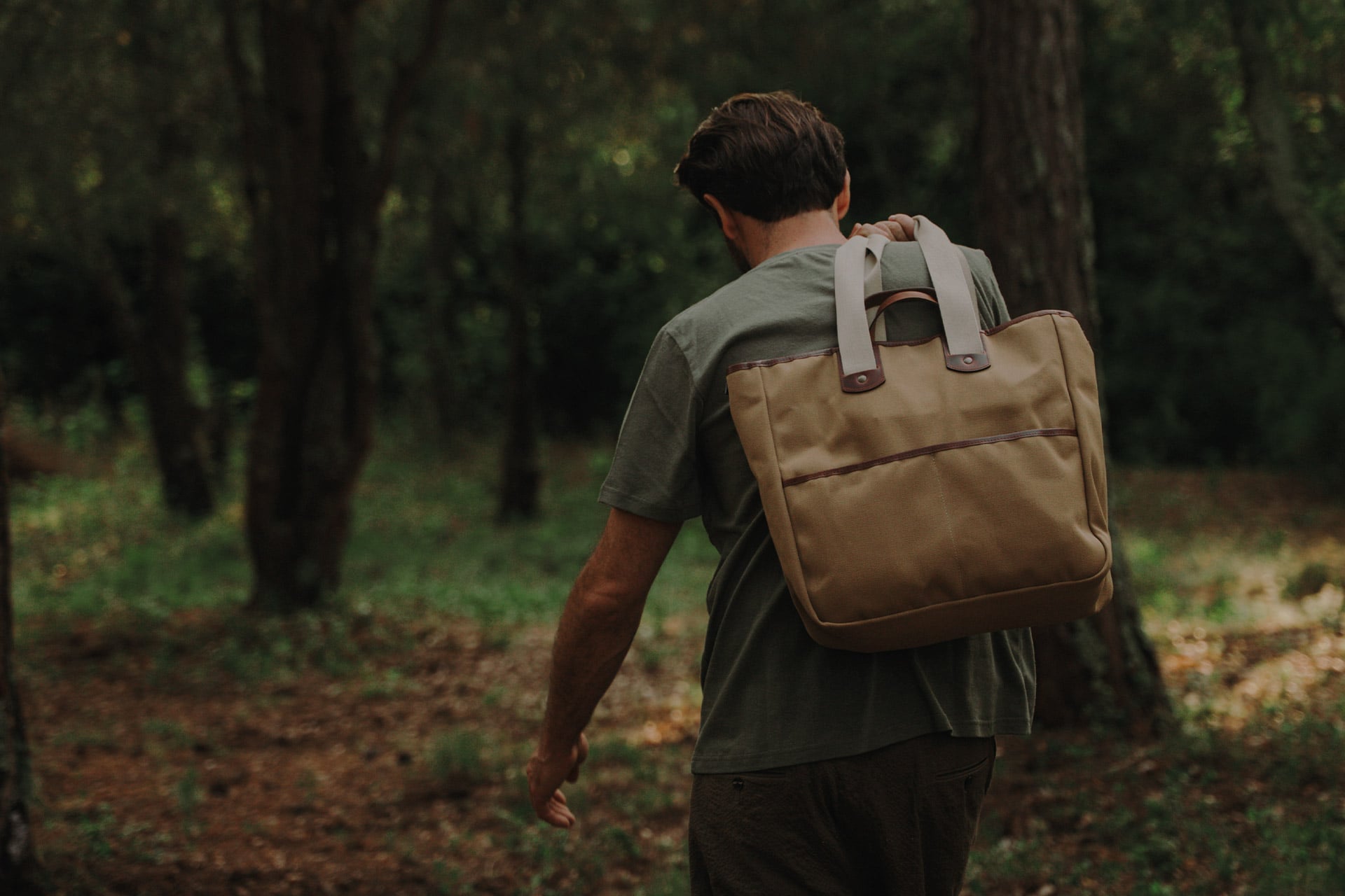 A man in the forest is wearing an organic t-shirt and a canvas tote bag over his shoulder