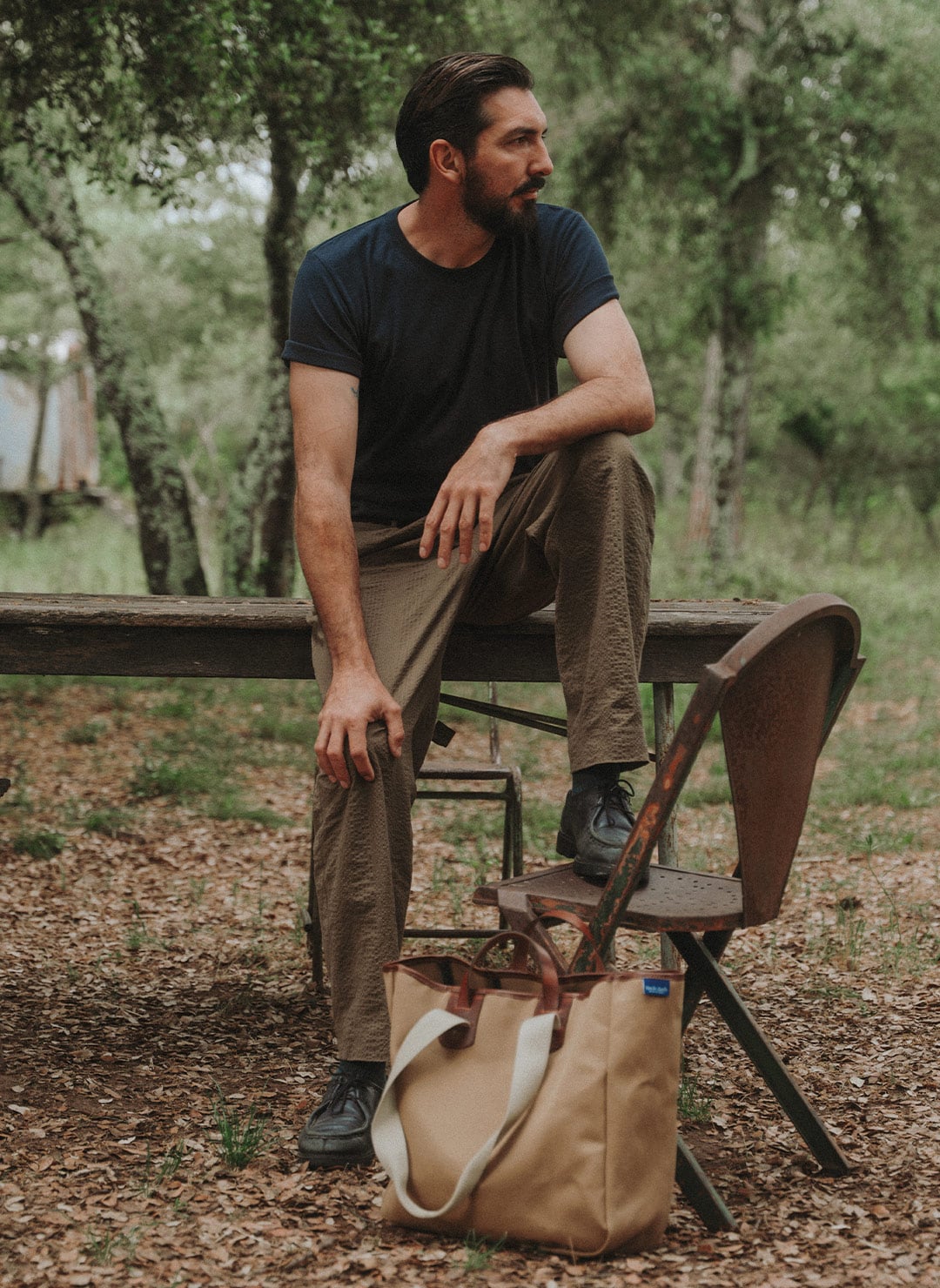 A man is posing in nature wearing his men's t-shirt and a tote bag