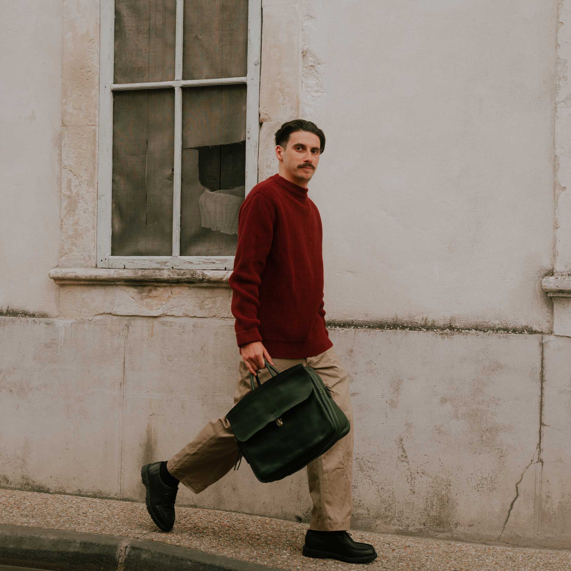 A man walks down the street carrying his men's leather work bag.