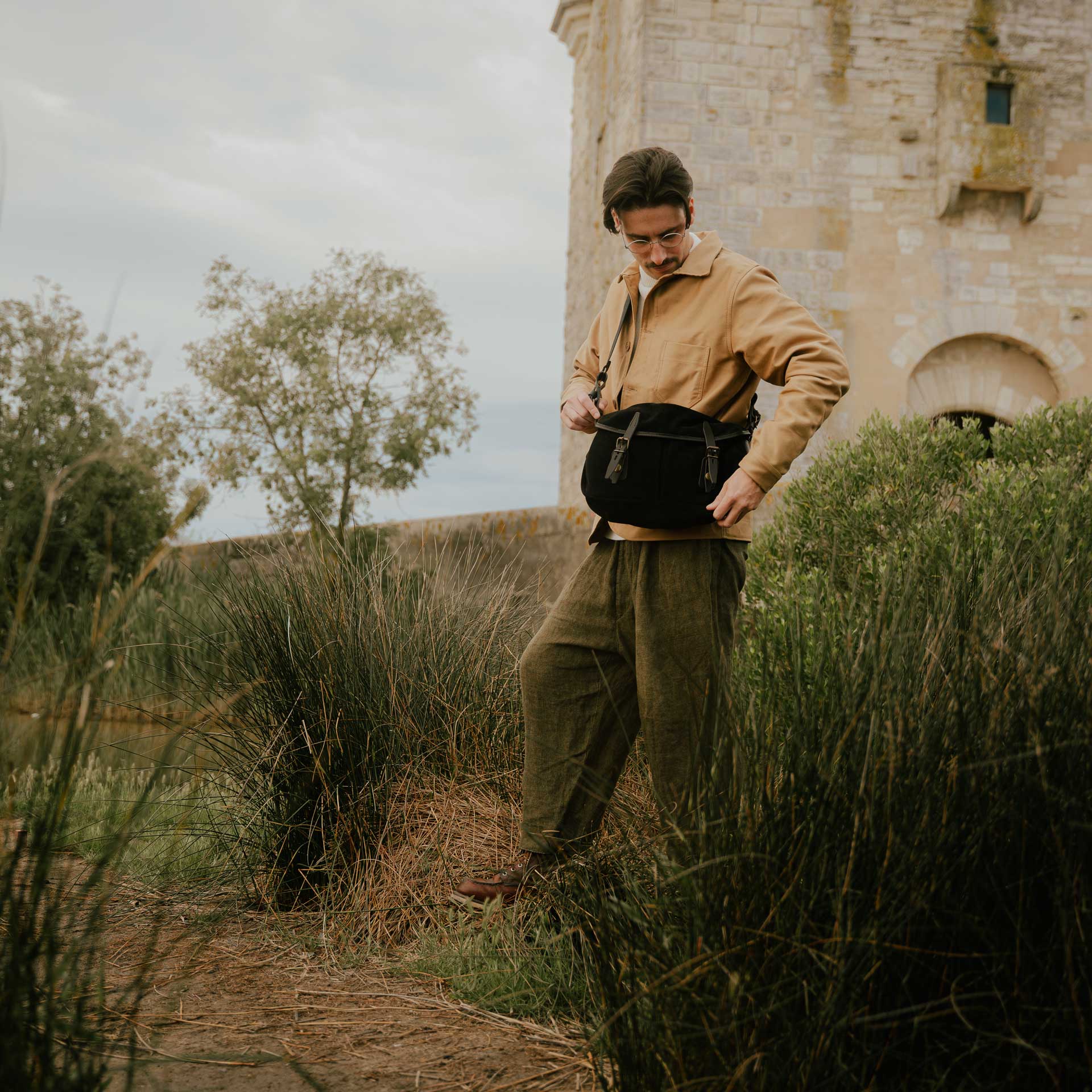A man outside in front of a ruin carries his black leather bag.