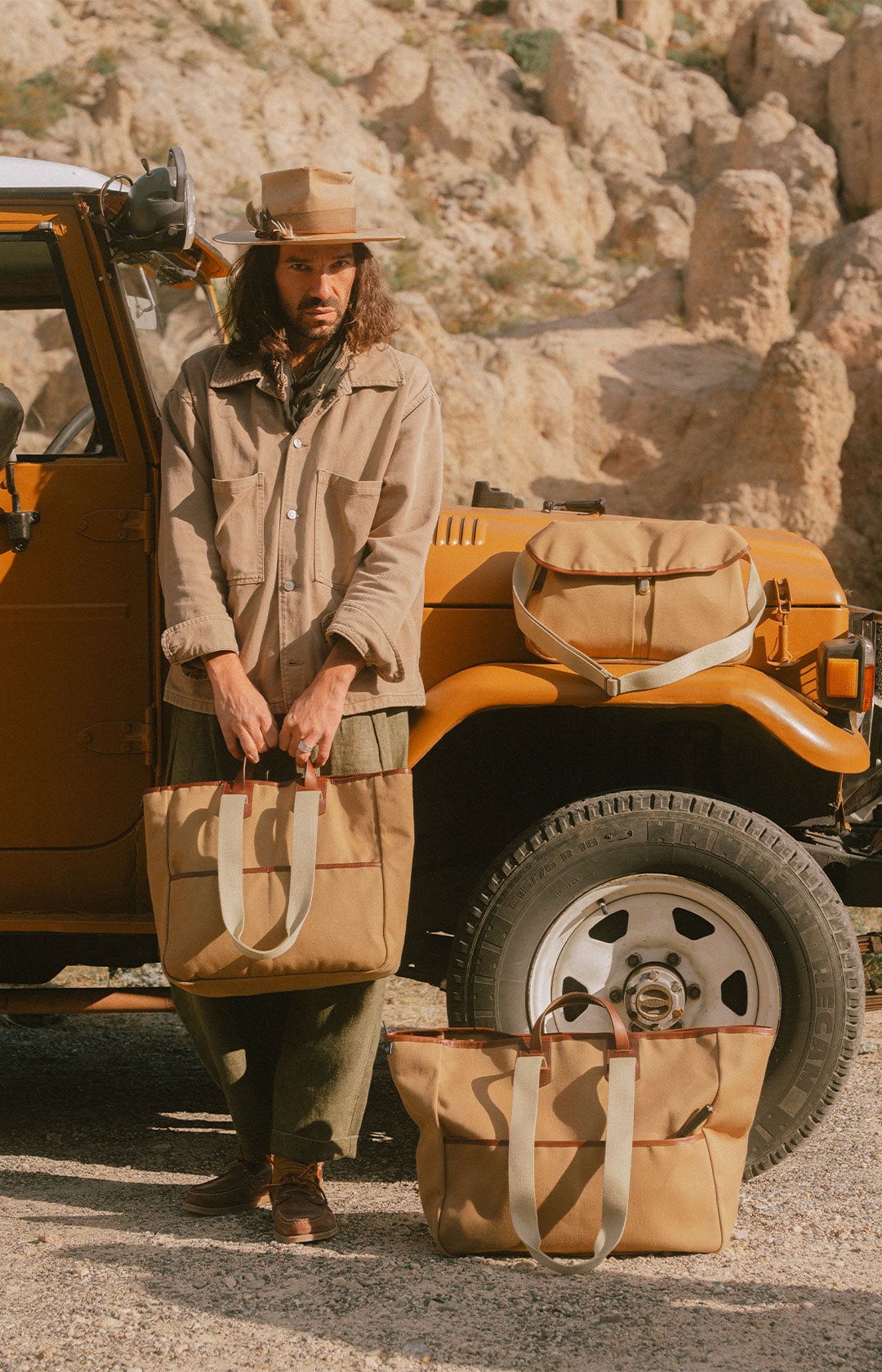 Un homme devant une jeep porte un cabas en toile. A cot&eacute; de lui sont pos&eacute;s deux autres sacs en toile.