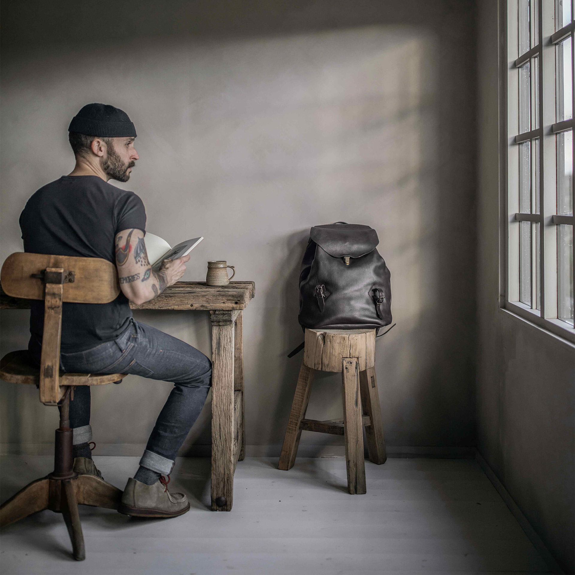 Un homme est assis &agrave; une table en bois, &agrave; cot&eacute; de lui, le sac ZIBELINE repose sur un tabouret