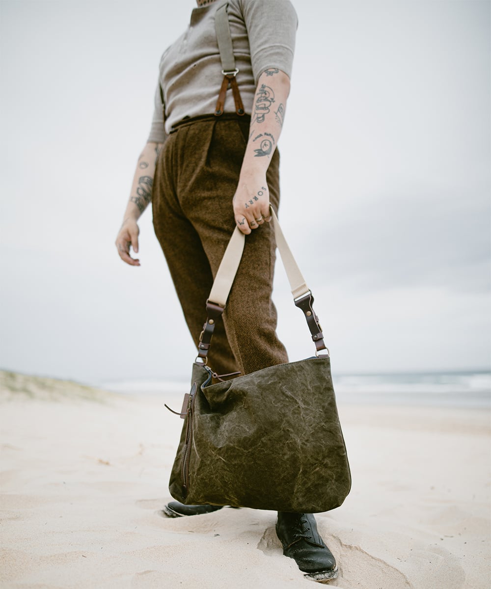 Un hombre en la playa sostiene su bolso masculino por la correa.