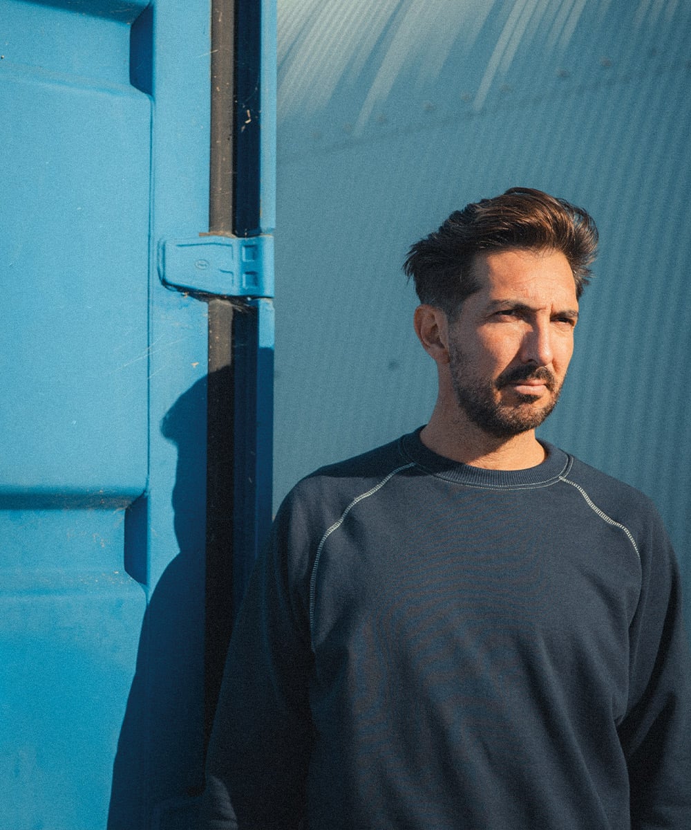Un homme porte un sweat bio coloris bleu devant un fond bleu