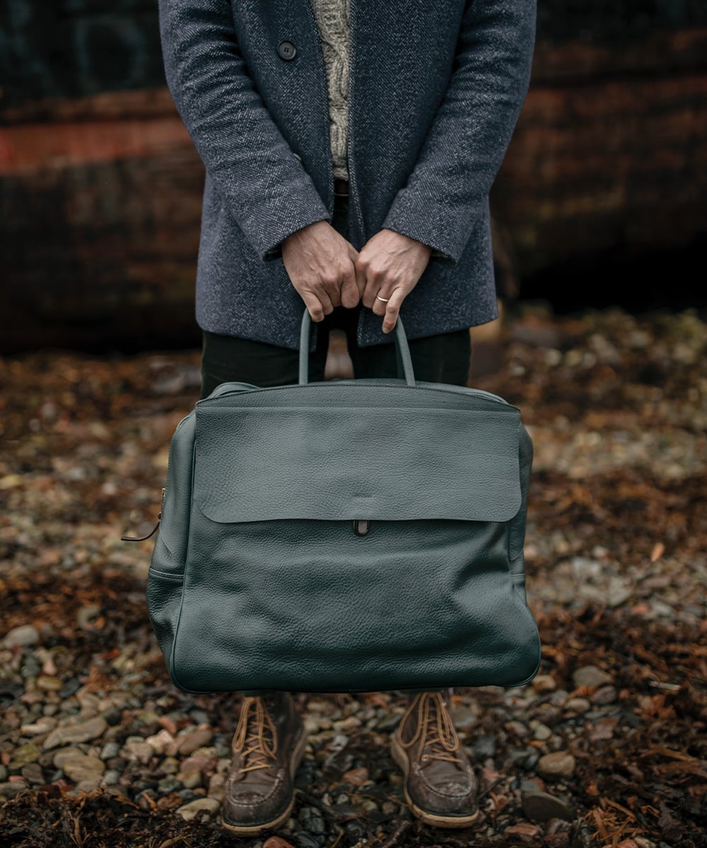 un homme tient devant lui un sac de voyage en cuir