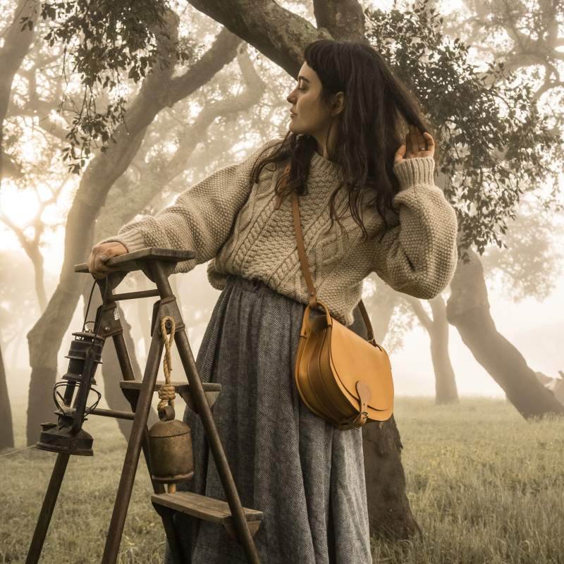 Une femme pose avec un sac en cuir dans une foret