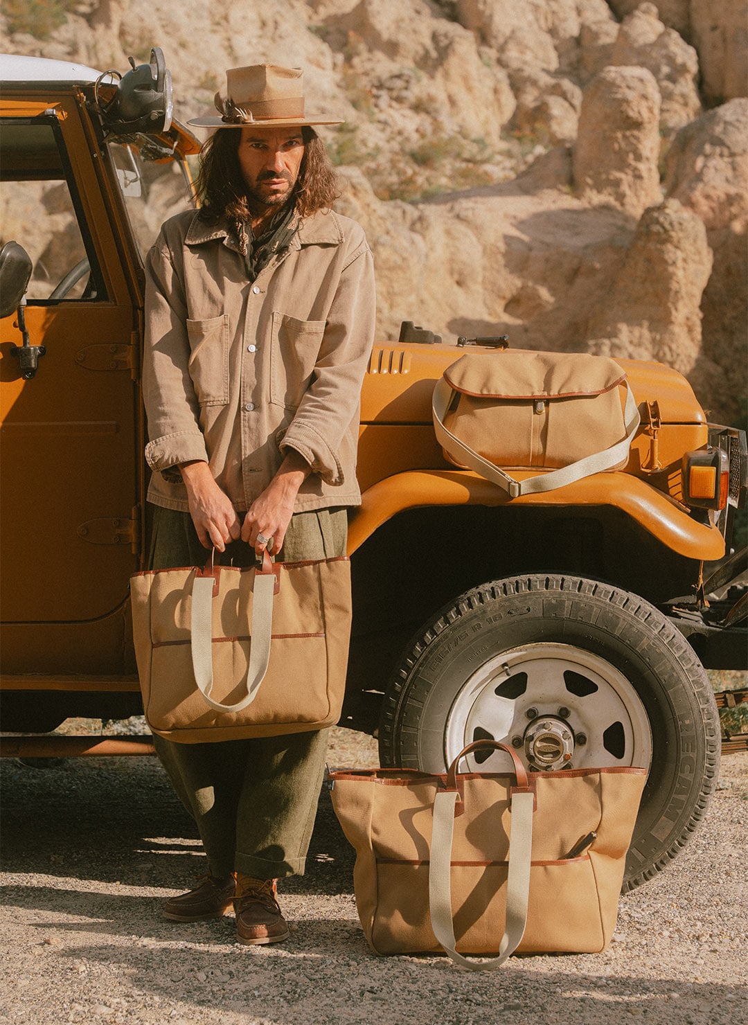 A man is standing in front of a Jeep, with three Bleu de Chauffe canvas bags displayed in front of him.